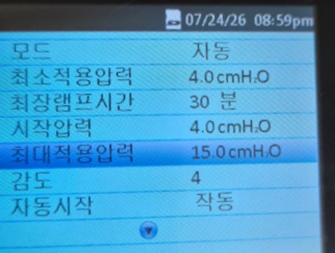 자동형 양압기 설정 화면 실물 사진 — 모드 자동, 최소적용압력 4.0cmH₂O, 최장램프시간 30분, 시작압력 4.0cmH₂O, 최대적용압력 15.0cmH₂O, 감도 4, 자동시작 작동으로 표시됨. 자동형은 최소와 최대 두 개의 압력값을 설정으로 받으며, 기기 화면에서 그 범위를 직접 확인할 수 있음